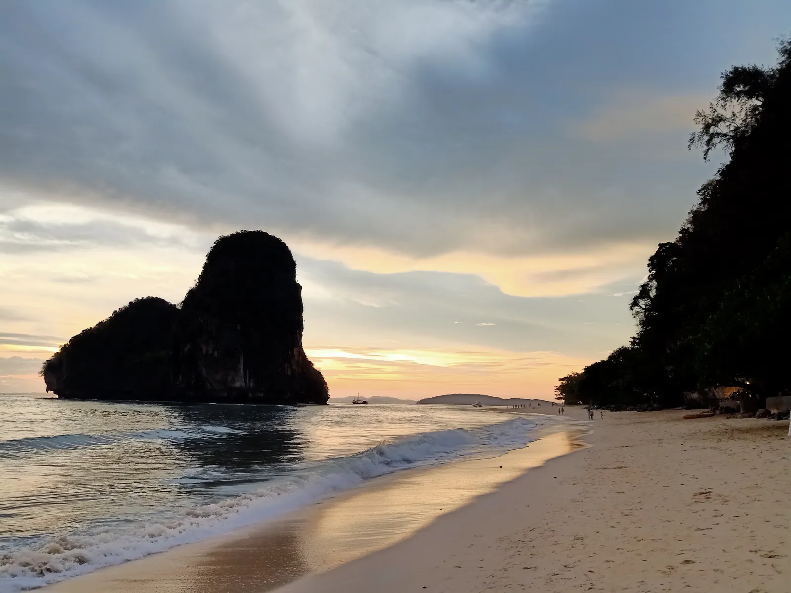 Uma rocha calcária a emergir do mar na Phra Nang Cave Beach ao pôr do sol, com areia molhada e uma falésia escura à direita
